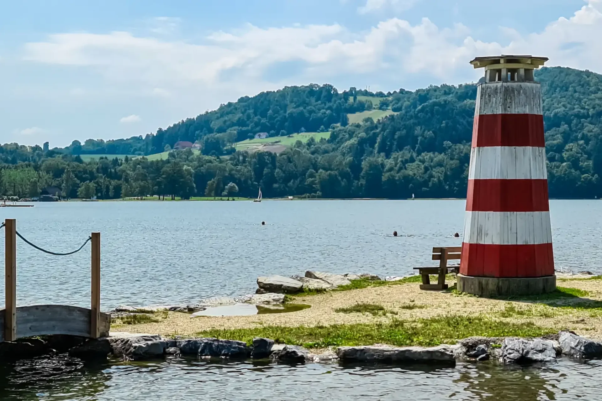 Charmanter-Leuchtturm-auf-einer-kleinen-Insel-die-durch-eine-Holzbruecke-am-Stubenbergsee-verbunden-ist