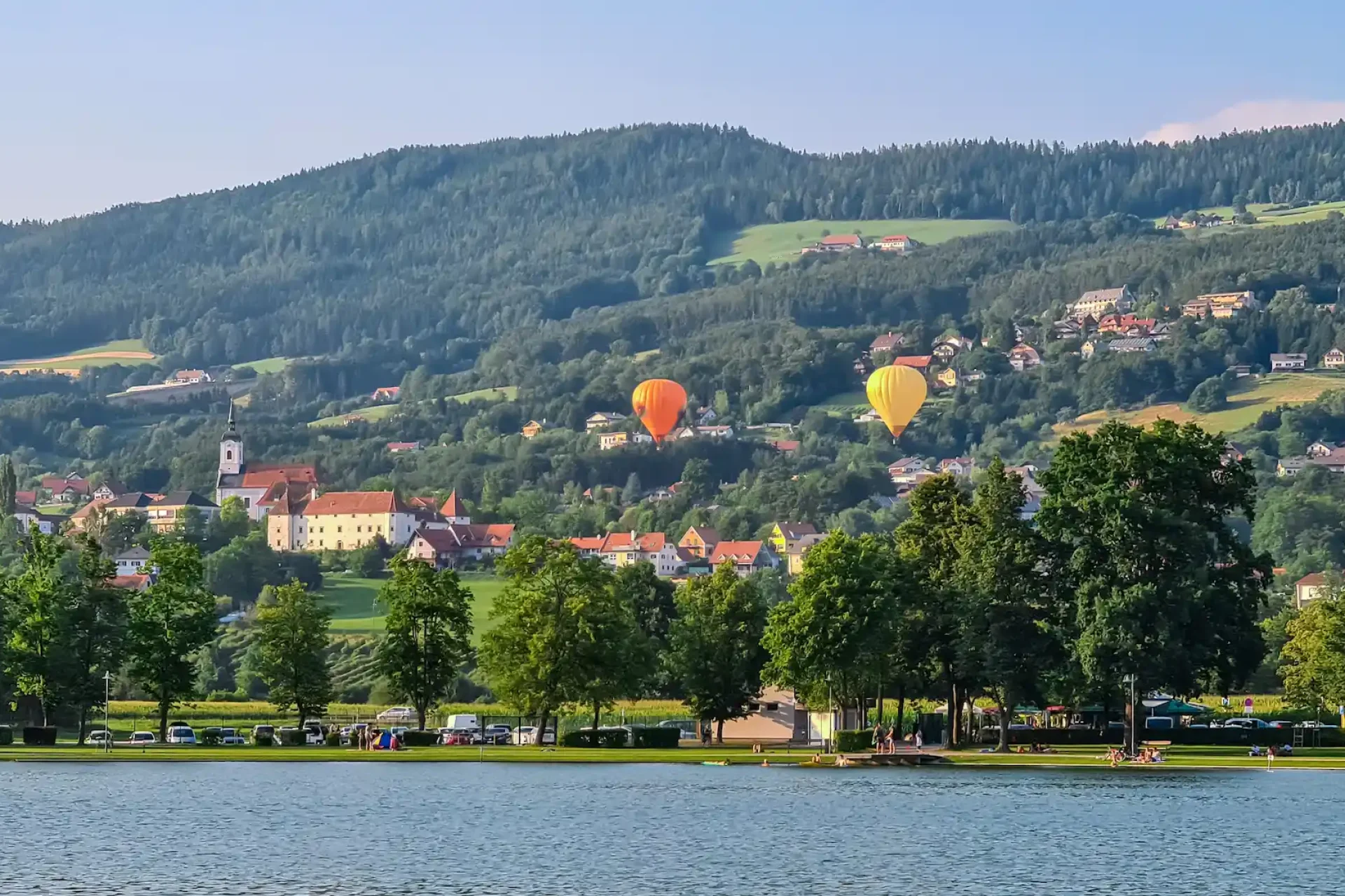 Zwei-farbenfrohe-Heissluftballons-schweben-anmutig-ueber-dem-Stubenbergsee